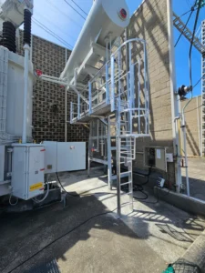 Travaux d'installation d'équipements de protection collective et individuelle sur un transformateur électrique haute tension par la sarl HTB Height Technician in Building ; systèmes antichute via échelle à crinoline avec passerelle avec garde-corps pour un accès sécurisé au transformateur, dans le cadre de travaux de sécurisation contre les chutes de hauteur