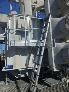 Intervention de la sarl HTB Height Technician in Building sur un transformateur électrique HTB pour l'installation d'équipements de protection collective et individuelle dans le cadre d'une opération de sécurisation contre les chutes de hauteur : passerelle avec garde-corps, support d'échelle (systèmes d'ancrage de sécurité)