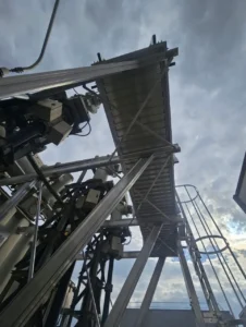 Vue en contre-plongée d'une passerelle aluminium avec garde-corps et échelle à crinoline, sur installation HTB (transformateur électrique, poste électrique RTE)