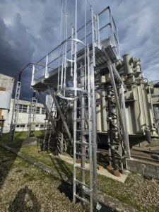 Installation d'équipement de protection collective pour les interventions de maintenance : passerelle avec garde-corps en aluminium avec échelle à crinoline devant un transformateur HTB, contre les risques de chute de hauteur