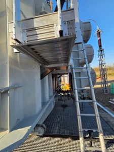 Intervention de Height Technician in Building sur un transformateur électrique pour la pose d'un équipement de protection collective. Il s'agit là d'installer une passerelle avec garde-corps dans le cadre de travaux de sécurisation contre les chutes de hauteur. La passerelle est munie d'un support d'échelle parallèle.