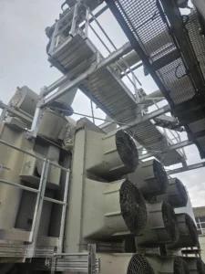 Intervention de Height Technician in Building sur un transformateur électrique pour la pose d'équipements de protection collective. Il s'agit là d'installer trois passerelles avec garde-corps dans le cadre de travaux de sécurisation contre les chutes de hauteur. Deux sont munies d'un support d'échelle parallèle, la dernière d'une échelle à crinoline.