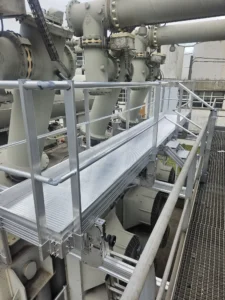 Intervention de Height Technician in Building sur un transformateur électrique pour la pose d'équipements de protection collective. Il s'agit là d'installer trois passerelles avec garde-corps dans le cadre de travaux de sécurisation contre les chutes de hauteur. Deux sont munies d'un support d'échelle parallèle, la dernière d'une échelle à crinoline.