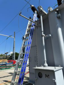 Intervention de la sarl Height Technician in Building pour l'installation de moyens d'accès sur transformateur électrique. Il s'agit en l'occurrence de mettre en place un support d'échelle perpendiculaire. Cela permet en effet à tout opérateur d'accéder à la partie haute de l'installation en toute sécurité. Intervention dans le cadre de travaux de sécurisation d'un transformateur électrique contre les chutes de hauteur.