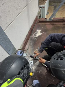 Intervention de Height Technician in Building pour la mise en place d'équipements de protection individuelle. Il s'agit là de mettre en place une ligne de vie câble. La ligne de vie câble est fixée au moyen de potelets, sur la toiture d'une enceinte insonorisée. Ce qui assure la sécurité de l'utilisateur lors de travaux en hauteur.