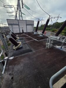 Intervention de Height Technician in Building pour la mise en place d'équipements de protection individuelle. Il s'agit là de mettre en place une ligne de vie câble. La ligne de vie câble est fixée au moyen de potelets, sur la toiture d'une enceinte insonorisée. Ce qui assure la sécurité de l'utilisateur lors de travaux en hauteur.